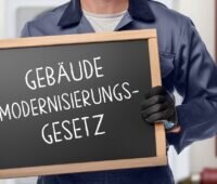 Ein Mensch hält eine Tafel mit der Aufschrift Gebäudemodernisierungsgesetz.