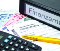 Ein Ordner, der mit Finanzamt beschriftet ist, davon Steuerunterlagen, ein Stift und ein Taschenrechner. Auch für die steuerliche Förderung ist Sachkenntnis erforderlich.