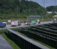 Im Vordergrund eine Freiflächen-PV-Anlage, im Hintergrund ein bewaldeter Hügel, dazwischen eine Autobahn. Deutschland reißt EU-Klimaziele.