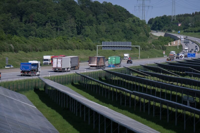 Im Vordergrund eine Freiflächen-PV-Anlage, im Hintergrund ein bewaldeter Hügel, dazwischen eine Autobahn. Deutschland reißt EU-Klimaziele.