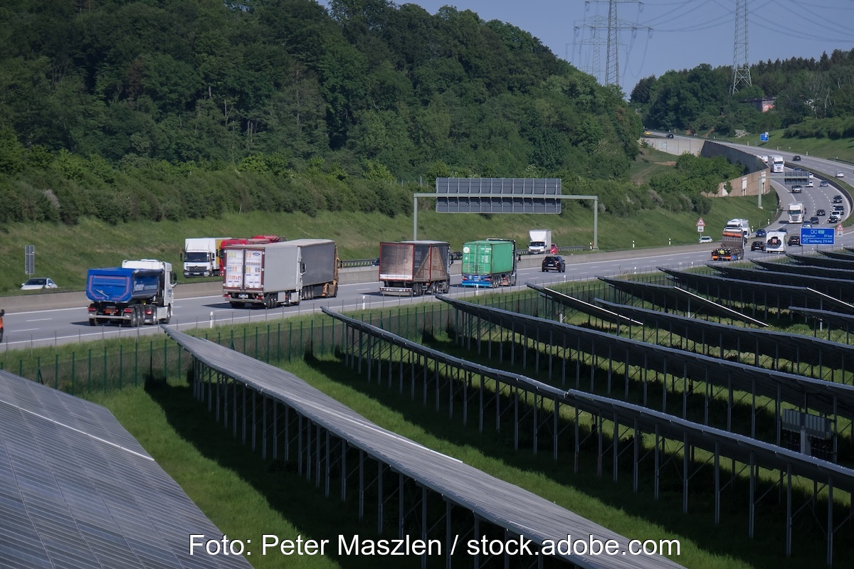 Im Vordergrund eine Freiflächen-PV-Anlage, im Hintergrund ein bewaldeter Hügel, dazwischen eine Autobahn. Deutschland reißt EU-Klimaziele.