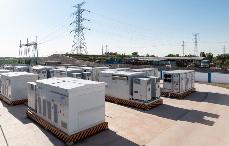 Batteriespeicher in Containern vor Stromleitungen, der BVES will Beschwerde bei der Europäischen Kommission gegen StromVKG einlegen, weil dieses Stromspeicher diskriminiert.