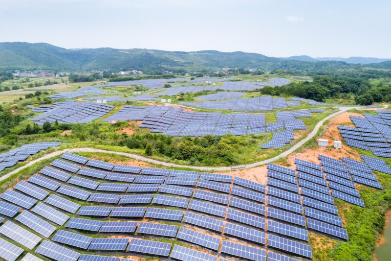 Aus der Vogelperspektive der Blick auf eine Hügellandschaft in China mit Photovoltaikanlagen, die von Büschen eingerahmt sind.