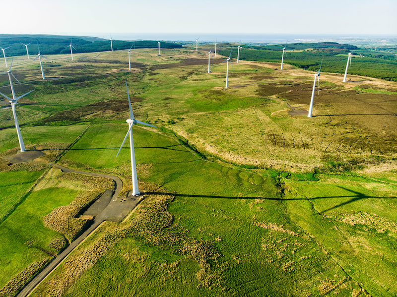 Luftaufnahme mit Windpark auf grünem Land - Windenergie in Irland. Batteriespeicher zur Netzstabilität sind dabei auch gefragt.