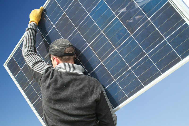 Ein Monteur trägt ein Photovoltaik-Modul.