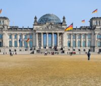 Ansicht des Bundestags, im Vordergrund die davor liegende Wiese. Vor dem Bundestag flanieren Menschen