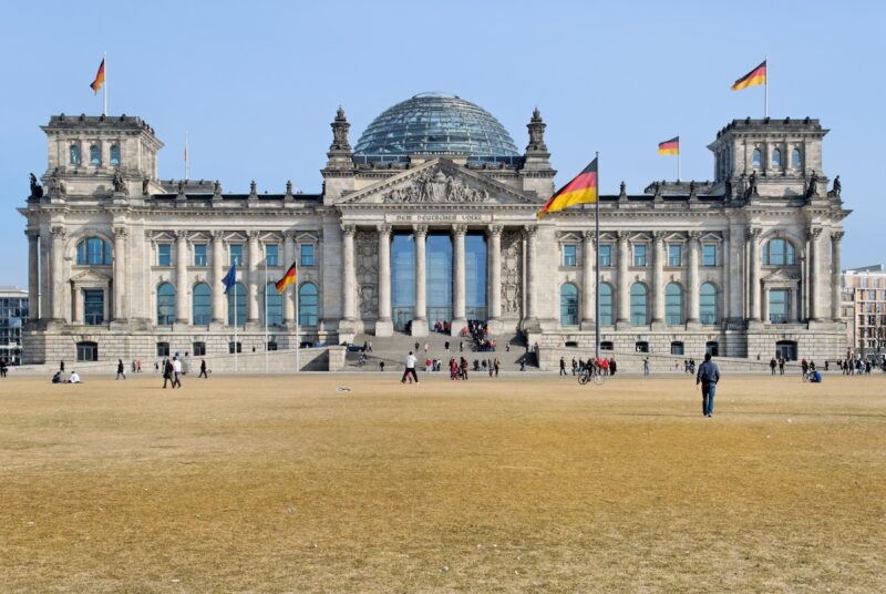 Ansicht des Bundestags, im Vordergrund die davor liegende Wiese. Vor dem Bundestag flanieren Menschen
