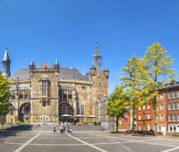 Das Rathaus von Aachen im Hintergrund, vorn ein Platz mit Gebäuden und Bäumen am Rand.