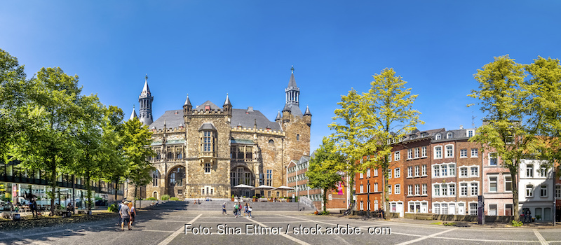 Das Rathaus von Aachen im Hintergrund, vorn ein Platz mit Gebäuden und Bäumen am Rand.