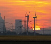 Energiewende. Windkraftanlagen vor Kohlekraftwerk und Strommasten. Ganz im Hintergrund die untergehende Sonne.