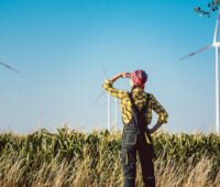 Ein Frau in Latzhosen schaut auf einen Windpark - Symbol für Bürgerenergie