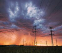 Sonnenuntergang mit durch Regenwolken verdunkeltem Himmel und Strommasten davor