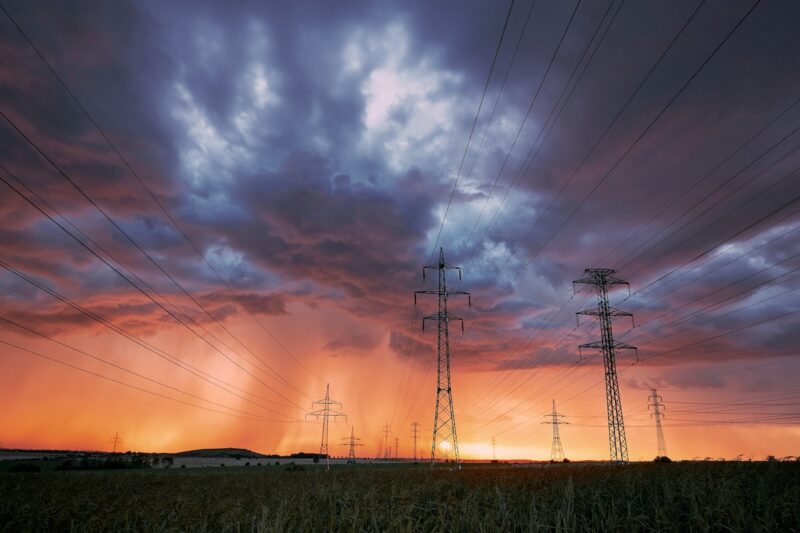 Grauer Himmel über Stromnetzen, am Horizont dringt die Sonne durch.