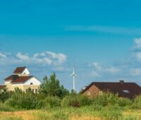 Im Vordergrund eine Wiese und Gebäude, im Hintergrund Windkraftanlagen