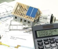Konstuktionszeichnungen von Gebäuden, darauf das Modell eines Hauses und ein Taschenrechner