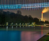 Nachstimmung im Oberhausen. Am oberen Bildrand eine beleuchtete Brücke über einem Kanal. Weiter hinten ein beleuchteter Schornstein.