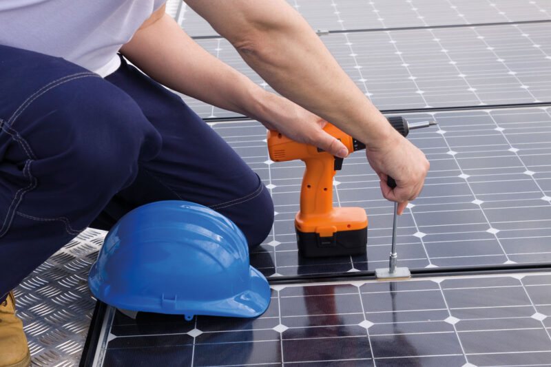 Handwerker verschraubt Photovoltaik-Module auf einem Dach