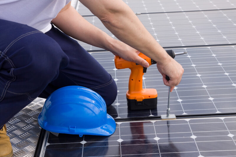 EIn Handwerker schraubt Photovoltaik-Module fest. Habecks Osterpaket mit dem EEG 2023 wirkt sich auf den weiteren Ausbau der Photovoltaik aus.