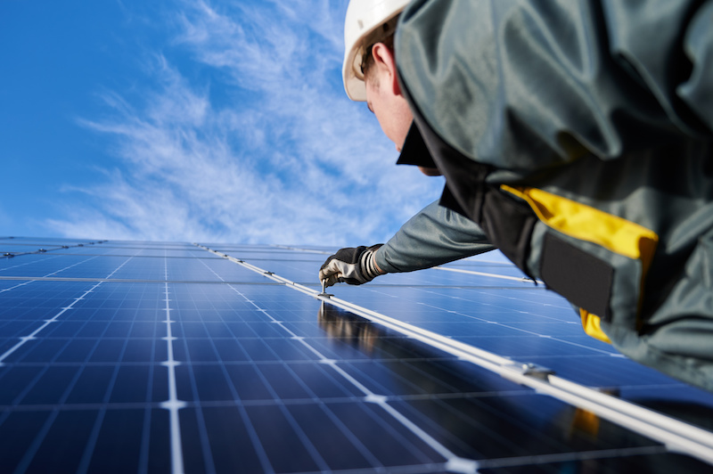 Solarinstallateur rechts vor Solarmodulen, die in die Höhe ragen.