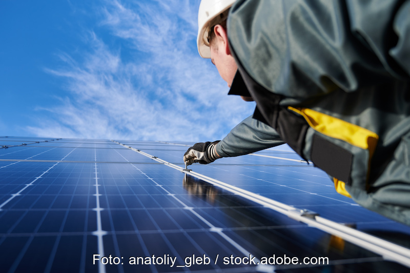 Solarinstallateur rechts vor Solarmodulen, die in die Höhe ragen.