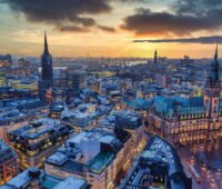 Luftbild einer Kommune (vermutlich Hamburg) im Sonnenuntergang mit beleuchteten Fenstern.