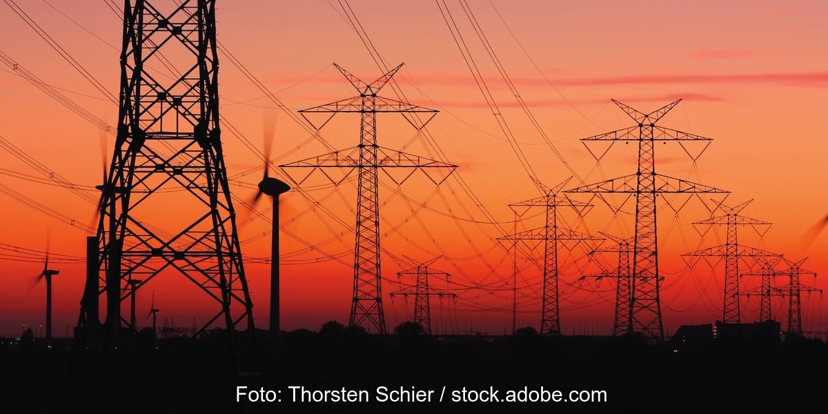 Strommasten von Hochspannungsleitungen bei Sonnenuntergang mit Windrädern.