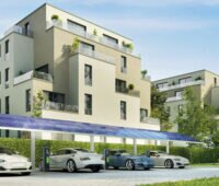 Im Hintergrund ein Mehrfamilienhaus, vorn Elektrofahrzeuge mit Ladestationen, die unter einem Carport mit Photovoltaikmodulen stehen.