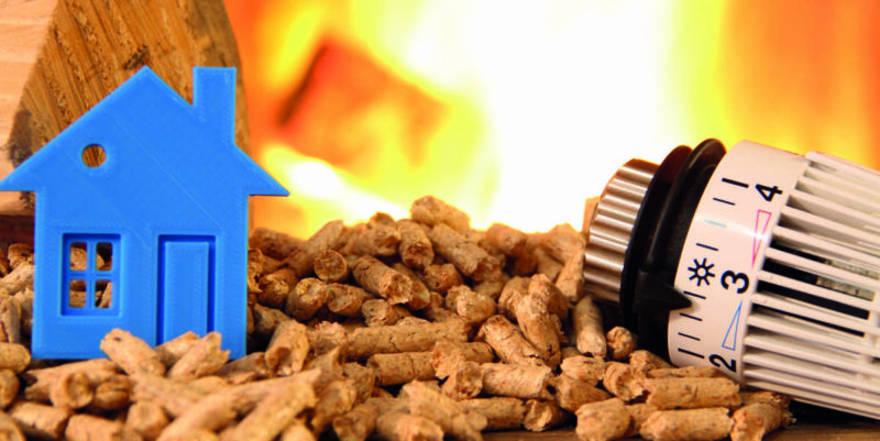 Symbolbild für Biomasse in der BEG-Förderung 2023:ein stilisiertes Haus steht links auf einem Haufen Holzpellets, rechts ein Thermostat, im Hintergrund lodern Flammen