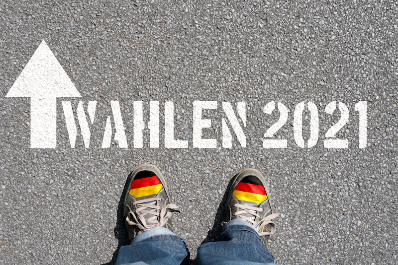Straßenbelag, auf den "Wahlen 2021" geschrieben wurde. Davor unten im Bild ein paar Schuhe. Bald ist Wahlkampf.
