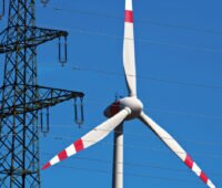 Windenergieanlage der Marke Enercon hinter einer Stromleitung mit langer Brennweite (Teleobjektiv) fotografiert. Symbolbild für CfD