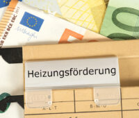 Ein Aktenordner mit der Aufschrift Heizungsförderung, im Hintergrund Geldscheine