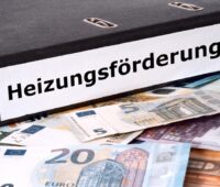Aktenordner mit der Aufschrift Heizungs-Förderung auf einem Haufen Geld.