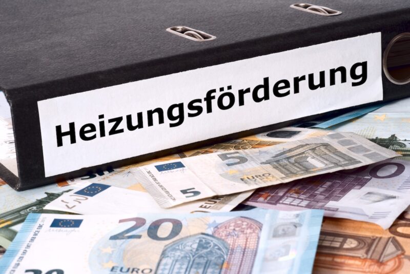 Aktenordner mit der Aufschrift Heizungs-Förderung auf einem Haufen Geld.