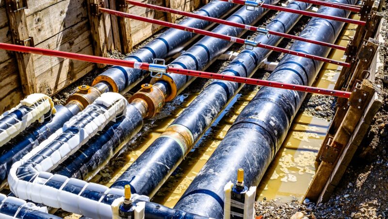 Vier große Fernwärmeleitungen in einer Baugrube, Power-to-Heat-Anlagen wie Großwärmepumpen und Elektrodenkessel sollten Elektrolyseuren bei Netzentgelten im AgNes-Verfahren gleichgestellt werden.