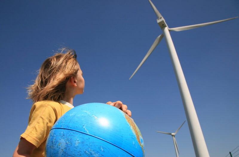 Ein junger Mensch schaut auf einen Windpark. In den Armen trägt er eine Weltkugel - Sinnbild für Bürgerenergie, Akzeptanz für Windenergie