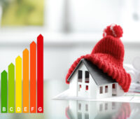 Illustration zu Bundesförderung effiziente Gebäude BEG - Gebäudeenergiegesetz: Links eine Grafik mit der Effizienzskala ab A, rechts das Modell eines Hauses unter einer Pudelmütze