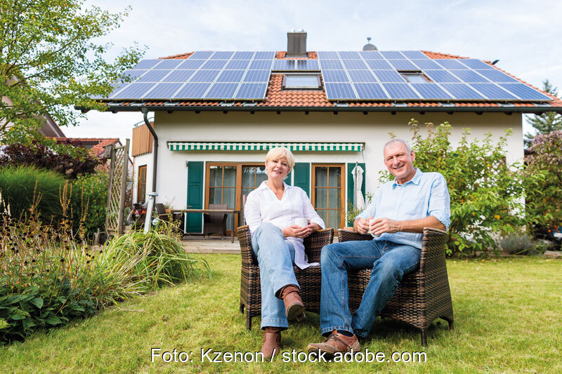Ein Paar sitzt im Garten vor einem Einfamilienhaus mit Photovoltaikanlage auf dem Dach.