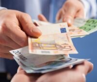 Hände von zwei Menschen beim Bezahlen mit Geldscheinen, das Anlagevermögen von Meyer Burger Germany geht in die Versteigerung.