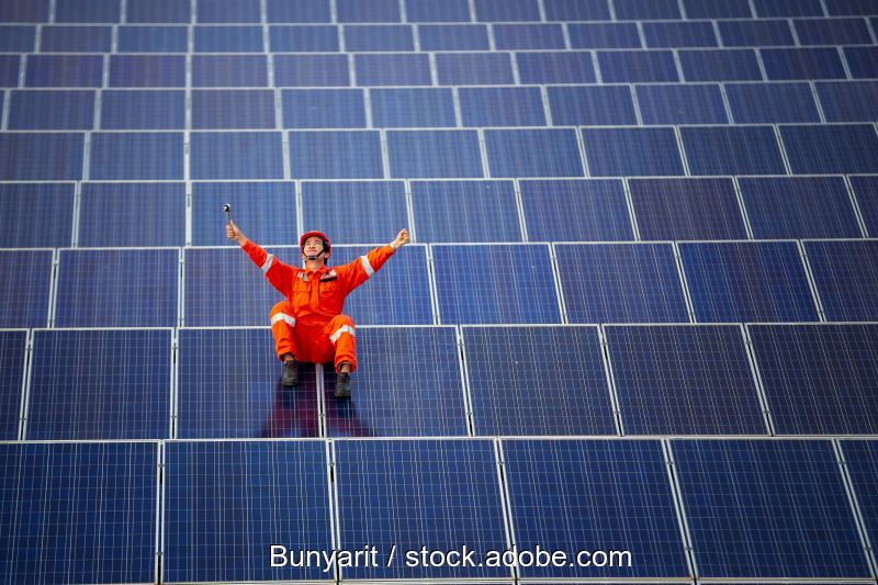 Arbeiter in freudiger Pose in einem Solarmodulfeld.