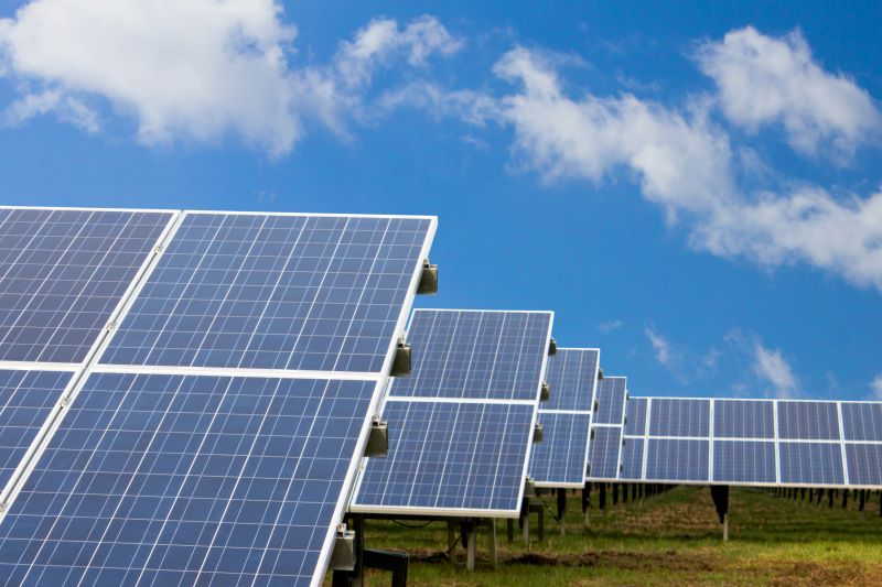 Eine Reihe von aufgeständerten Solarmodulen unter blauem Himmel mit einzelnen Wolken.