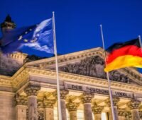 Beleuchtetes Gebäude des Deutschen Bundestages mit Europa- und Deutschlandflagge im Vordergrund.