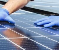 Zwei Hande mit Schutzhandschuhen bei der Handhabung von Solarmodulen.