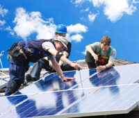 Drei Handwerker auf dem Dach montieren Photovoltaik.