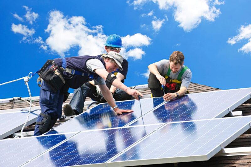 Drei Handwerker auf dem Dach montieren Photovoltaik.