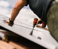 Handwerker montiert mit Akkuschrauber eine Photovoltaik-Anlage auf einem Ziegeldach.