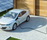 Ein E-Fahrzeug vor der Garage wird geladen mit PV-Anlage daneben.