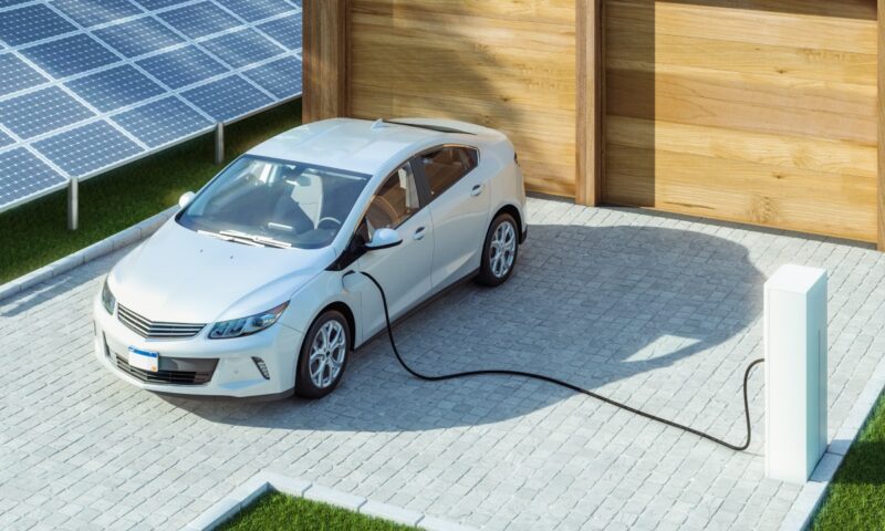 Ein E-Fahrzeug vor der Garage wird geladen mit PV-Anlage daneben.