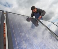 Ein Installateur befestigt Solarmodule auf einem Schrägdach.