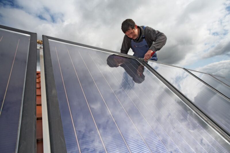 Ein Installateur befestigt Solarmodule auf einem Schrägdach.