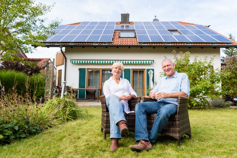 Ein Paar sitzt im Garten vor einem Einfamilienhaus mit Photovoltaikanlage auf dem Dach.